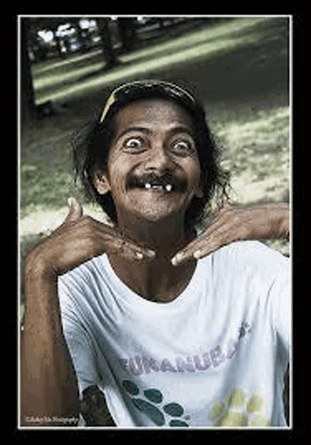 a man with a mustache and missing teeth is making a funny face while wearing a white shirt .