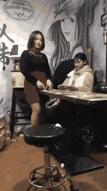 two women are sitting at a table in front of a painting of a woman