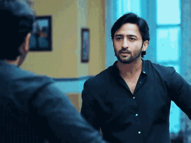 a man in a black shirt is looking at his reflection in the mirror