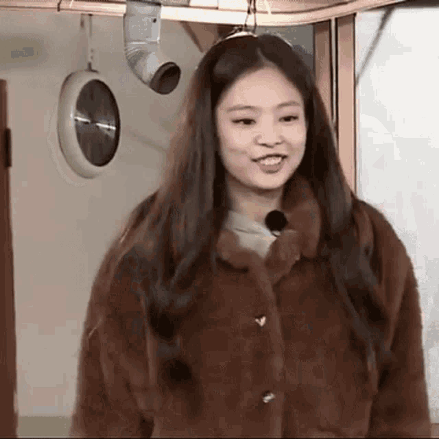 a woman in a fur coat is standing in a room with a clock hanging on the wall .