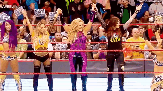a group of female wrestlers are standing in a ring holding hands .