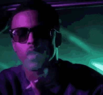 a man wearing sunglasses and headphones is smoking a cigarette in a club .