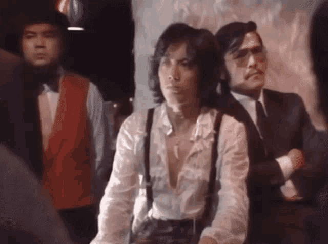 a man in a white shirt and suspenders stands in a crowd of men