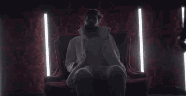a man in a white coat is sitting on a red couch in a dark room .