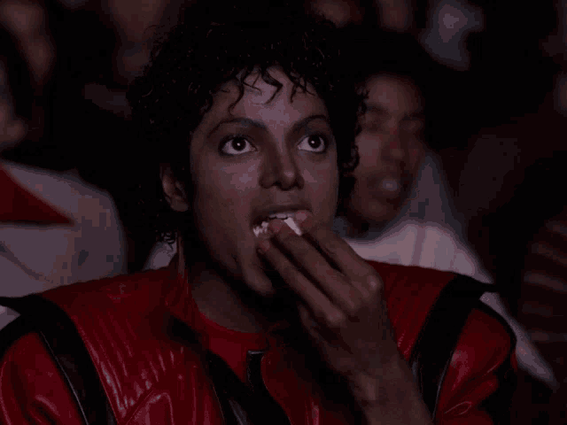 a man in a red and black jacket is eating popcorn