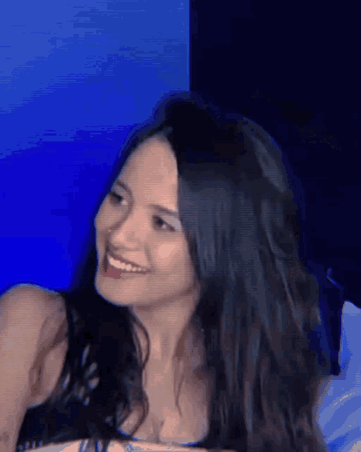 a woman with long black hair is smiling in front of a blue wall