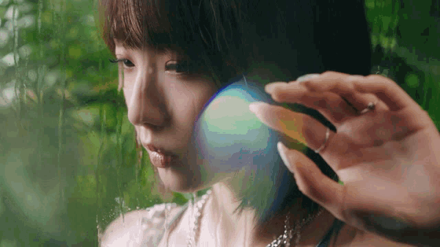 a woman with a ring on her finger is holding a rainbow colored object in front of her face