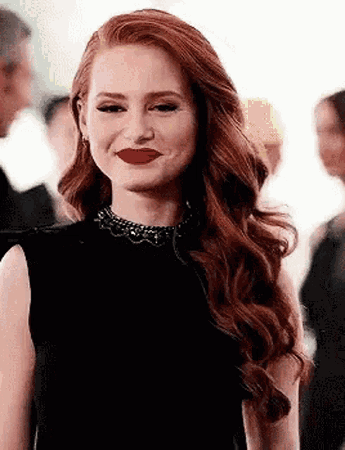 a woman with red hair and red lipstick is wearing a black dress and a necklace .