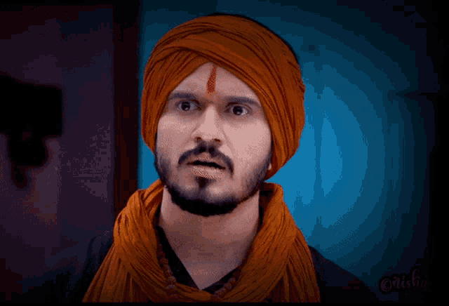 a man with a turban and a ring on his finger holds his finger to his mouth