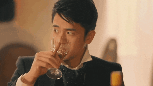 a man in a suit and bow tie drinking from a glass