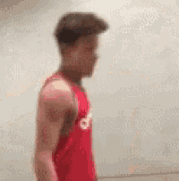 a young man in a red tank top is standing in front of a wall .