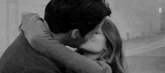 a black and white photo of a man and woman kissing .