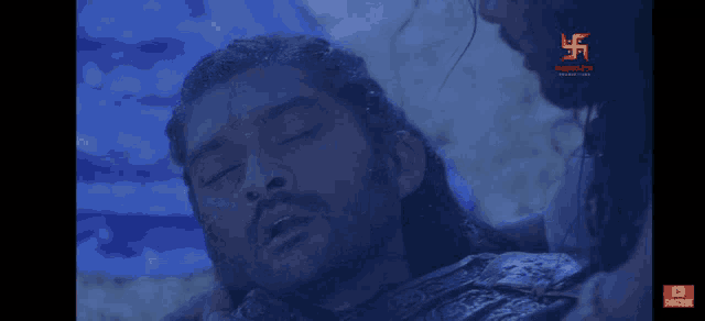 a man with a beard is laying on the ground with his eyes closed while another man holds his head