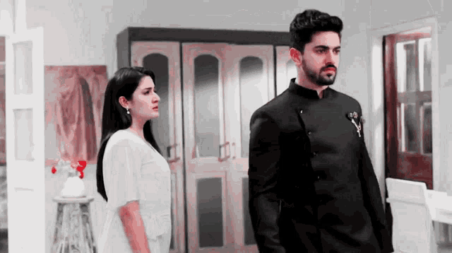 a man in a black suit and a woman in a white dress are standing next to each other in a room .