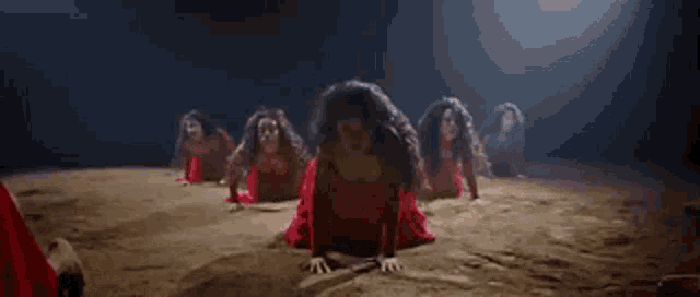 a group of women in red dresses are kneeling down in a dark room .