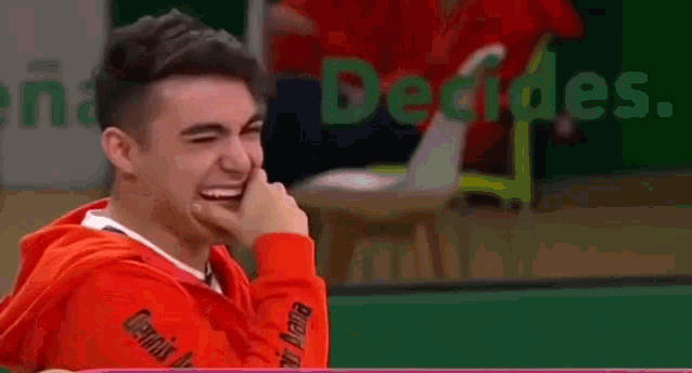 a young man in a red hoodie is laughing while sitting at a table .