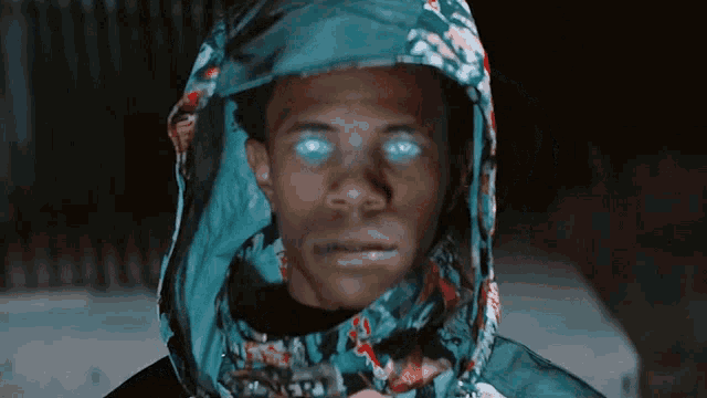 a man wearing a hooded jacket with blue eyes looks at the camera