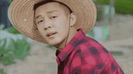 a young man wearing a straw hat and a plaid shirt .