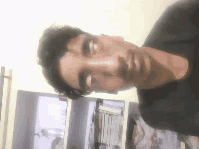 a man 's face is shown from above with a bookshelf in the background