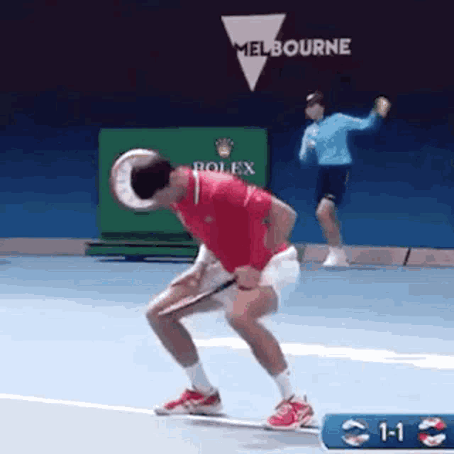 a man is holding a tennis racquet on a tennis court while another man throws a tennis ball .