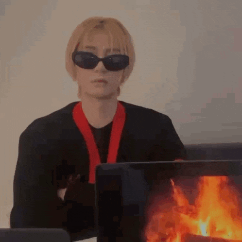 a man wearing sunglasses and a red scarf is sitting in front of a computer monitor with a fire on it .