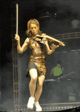 a woman in a gold dress is playing a violin on stage