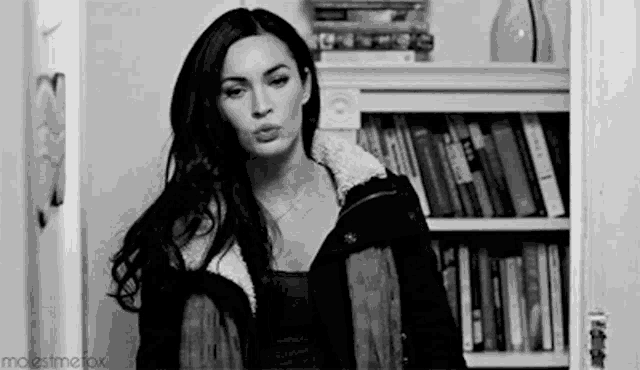 a woman is blowing a kiss in a black and white photo while standing in front of a bookshelf .