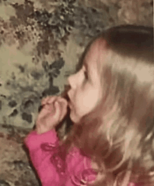 a little girl in a pink jacket is sitting on the floor eating a chocolate bar .