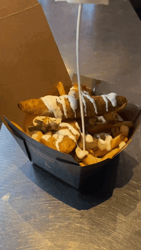 a box of french fries with a sauce being poured on it