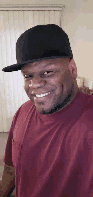 a man wearing a red shirt and a black hat is smiling