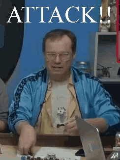 a man in a blue jacket sits at a table with a laptop and a sign that says attack on it