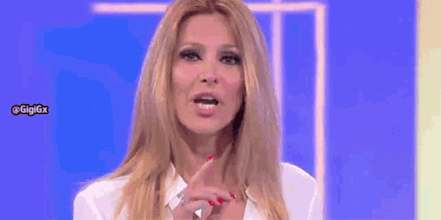 a woman with long blonde hair and red nails is making a funny face while talking on a television show .