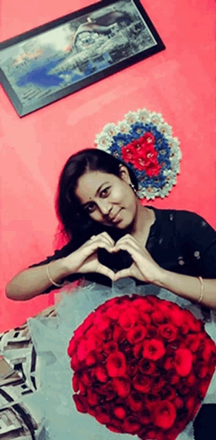 a woman makes a heart shape with her hands in front of a bouquet of red roses