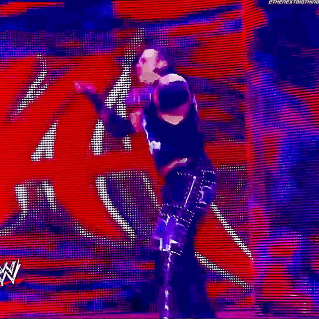 a wrestler is standing on a stage with his arms in the air in front of a red background .