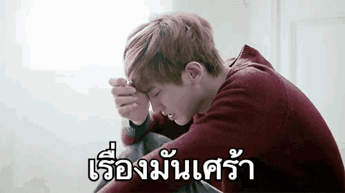 a young man in a red sweater is sitting on the floor with his head in his hands and crying .