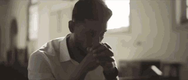 a man in a white shirt is praying with his hands folded in front of his face .
