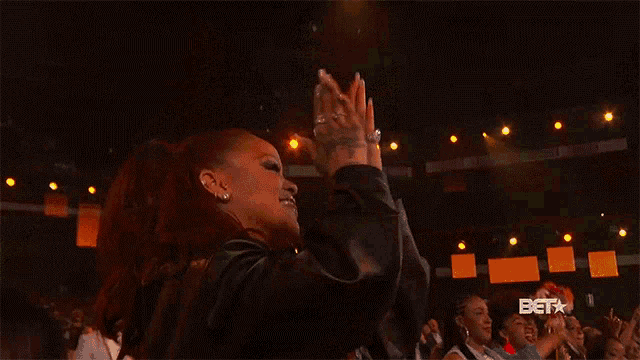 a woman with red hair is dancing in front of a crowd with the bet logo in the background .
