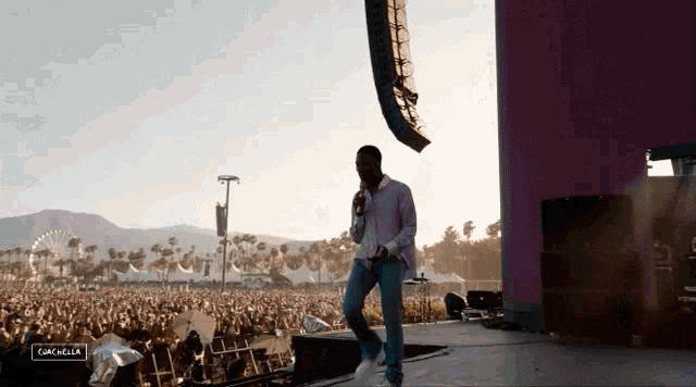 a man stands on a stage with a microphone in front of a crowd at a music festival and the word coachella is visible