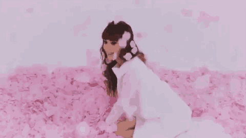 a woman in a white dress is kneeling down in a field of pink petals .