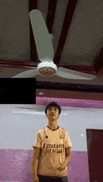 a boy wearing an emirates jersey stands in front of a fan