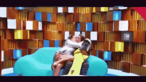 a man and woman are sitting on a blue couch in front of a wall with boxes on it