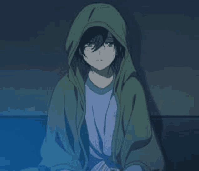 a boy in a green hoodie is sitting on a couch in a dark room .