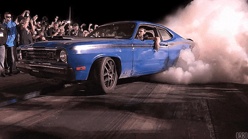 a blue car with smoke coming out of it is being photographed by a crowd