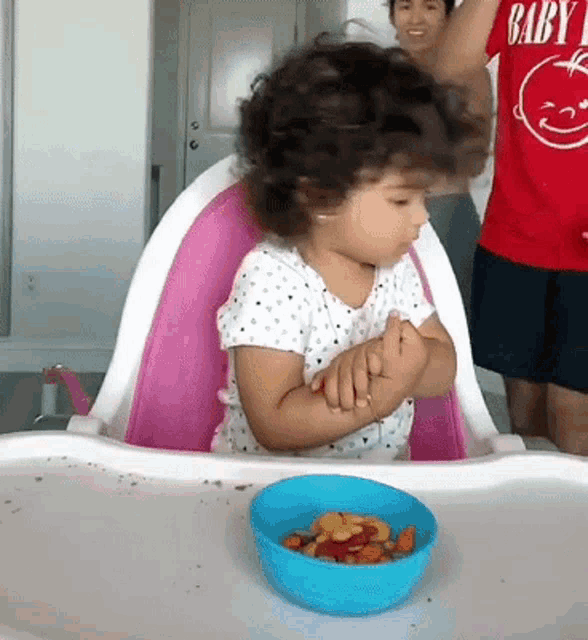 a little girl is sitting in a high chair eating from a blue bowl of fruit