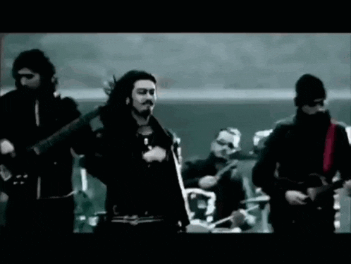 a man with long hair and a beard is standing in front of a group of men playing instruments .