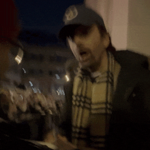 a man wearing a hat and scarf stands in front of a crowd of people