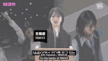 a woman speaking into a microphone with the name nmixx on the front