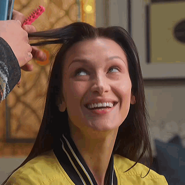 a woman in a yellow jacket is smiling while having her hair brushed