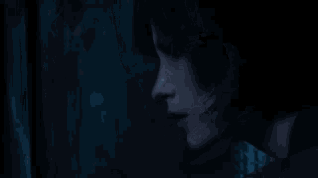 a close up of a woman 's face in a dark room looking out a window