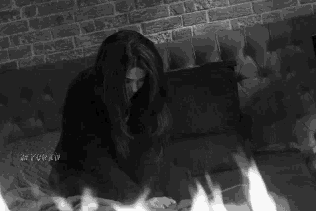 a black and white photo of a woman sitting on a couch with flames behind her